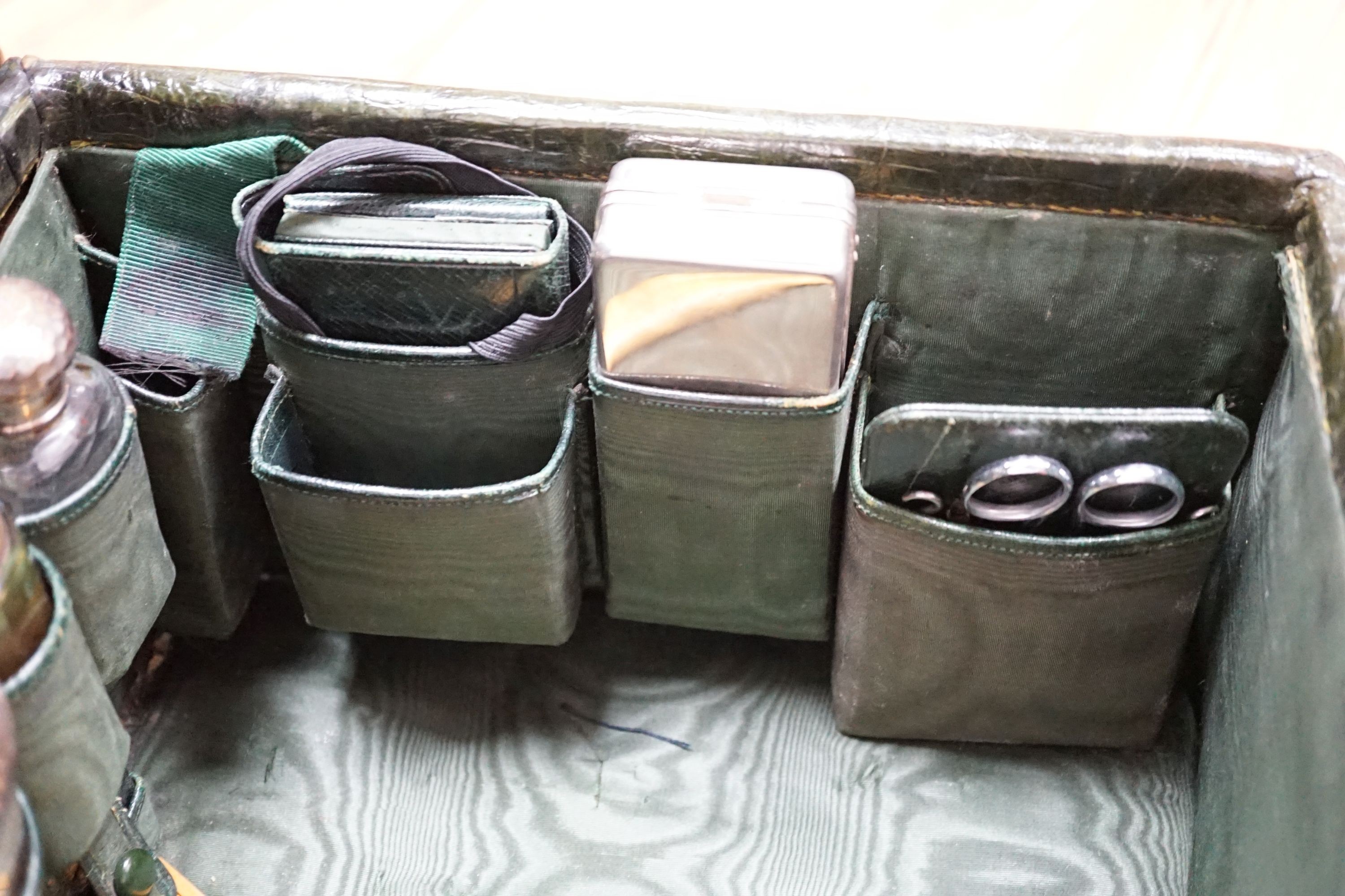 An early 20th century green crocodile toilet case with silver mounted interior, width 39 cms.